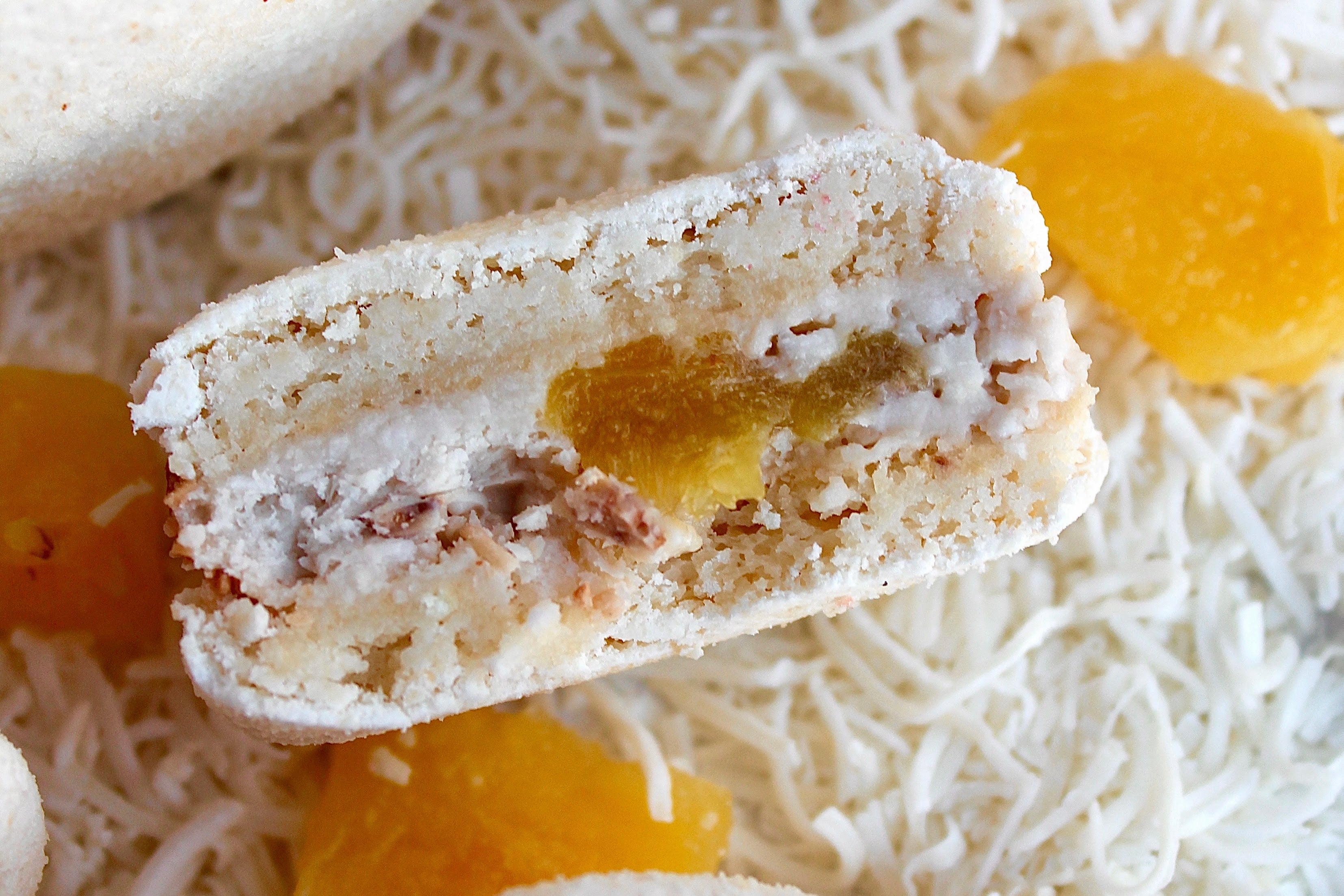 White macaron with coconut cream and pineapple filling, surrounded by shredded coconut and pineapple pieces. Dairy-free and gluten-free.